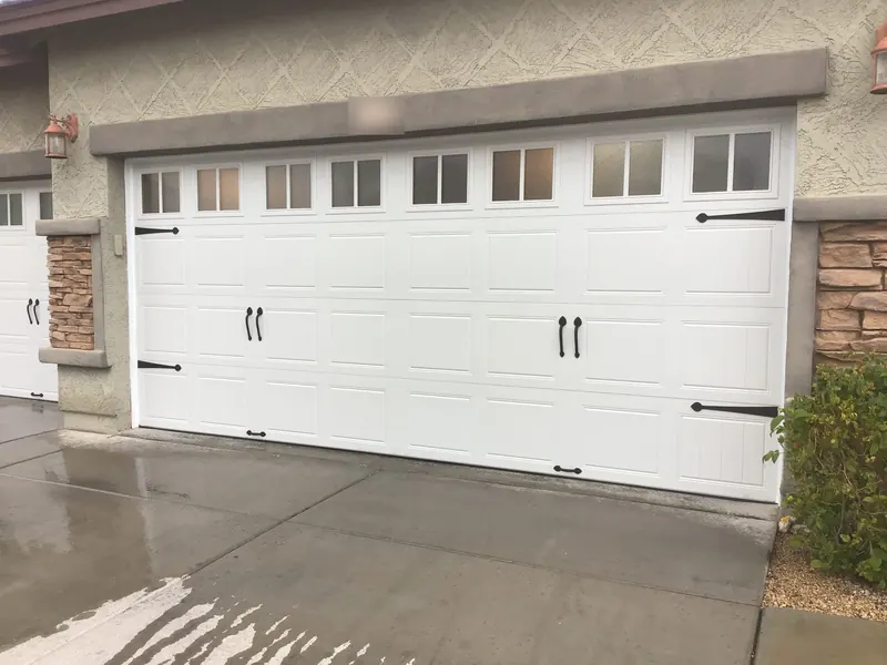 White carriage-house style garage door with windows and decorative hardware